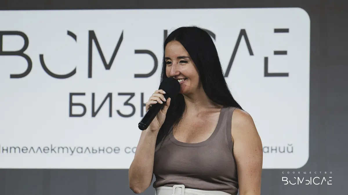 Ведущая демо-дня с микрофоном у экрана с логотипом «ВСмысле Бизнес»